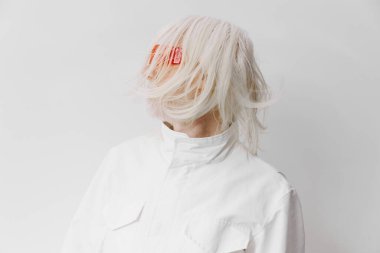 Koyu kırmızı saç tokalarıyla süslenmiş çarpıcı beyaz saçlı ileri model, modern tarz ve yaratıcılığı vurgulayarak sade bir arka plana karşı çağdaş bir görünüm sergiliyor.