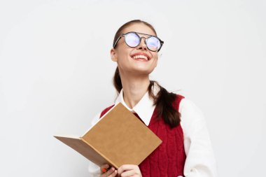 Gözlüklü neşeli genç bir kadın elinde bir defter tutuyor ve gülümsüyor, düz beyaz bir arkaplanda duruyor. İfadesi yaratıcılık ve coşku taşıyor, eğitim ve iş teması için mükemmel.