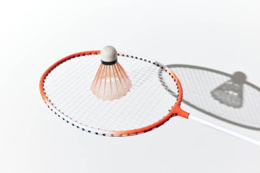 Badminton raketi ve beyaz yüzeyde gölgeli bir mekik. turuncu ve beyaz renk şeması.