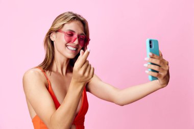 Mayo giymiş güzel genç bir kadın canlı pembe bir arka planda telefonuyla selfie çekiyor.