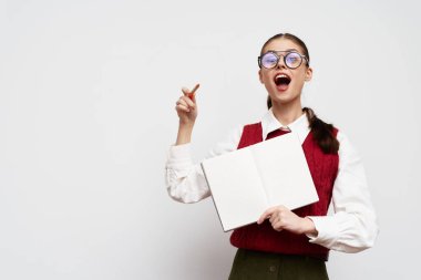 Heyecanlı, gözlüklü ve kırmızı yelekli bir kadın yukarıyı işaret ederken boş bir defter tutuyor, ilham ve yaratıcılığı simgeliyor.