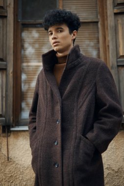 Kahverengi ceketli moda adamı, elleri ceplerinde pencerenin önünde dikiliyor, yan tarafa bakıyor..