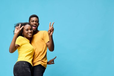 Aynı sarı tişörtleri giyen neşeli genç çift, mutluluk ve dostluğu canlı mavi bir arka plana karşı ifade ediyor, arkadaşlık ve kutlama teması için ideal.