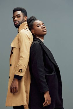 Çağdaş paltolar giyen, kendine güvenen ifadelerle sırt sırta verip gri bir zemin hazırlayan, yaşam tarzı ve moda kavramları için mükemmel bir çift.