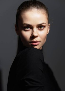 Siyah balıkçı yaka kazak içinde zarif ve kendine güvenen çarpıcı bir kadın modeli. Karanlık arka plan, güzelliğini ve gücünü vurgulayarak onun özelliklerini vurguluyor..