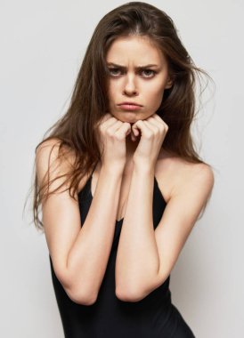 Yoğun bir ifadeye sahip genç bir kadın, uzun dalgalı saçlar, ve uygun siyah bir kıyafet, nötr bir geçmişe karşı hüsran ve kararlılık duygularını iletiyor..