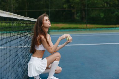 Spor kıyafeti giyen bayan tenisçi tenis kortunda poz veriyor. Konsantrasyon ve azim gösteriyor. Sezonluk spor yaşam tarzını yansıtıyor.