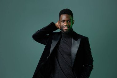 Zarif siyah kıyafetli Afro-Amerikan erkeği canlı yeşil arka plana karşı duruyor, çağdaş tarz ve zarafeti somutlaştırıyor..