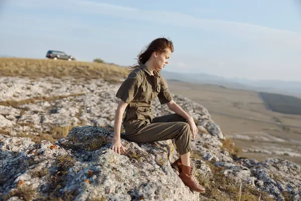 Uzak araba yolculukları ve dağlardaki macera konseptiyle kayada oturan kadın.