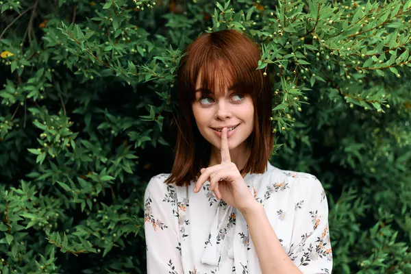 Gizem ve tefekküre dalmış kızıl saçlı kadın çalıların önünde duruyor.