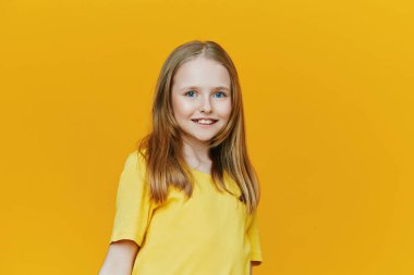 Sarı tişörtlü parlak ve neşeli genç bir kız. Sıcak sarı bir arka plan önünde mutluluk ve pozitiflik yayıyor. Mevsimsel ve motivasyon için ideal.