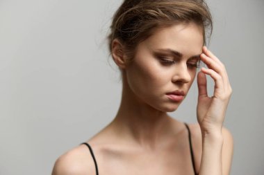 Doğal makyajı ve basit kıyafetleri olan sakin bir genç kadın, düşüncelere dalmış, incinebilirlik ve içgözlem duygusunu minimalist bir ortamda somutlaştırıyor..