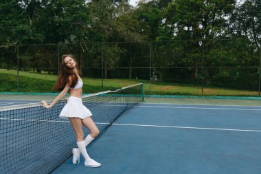 Sahada poz veren, spor için enerji ve tutku sergileyen, fitness veya aktif yaşam tarzı kavramları için ideal, beyaz tenis kıyafetli mutlu genç kadın.