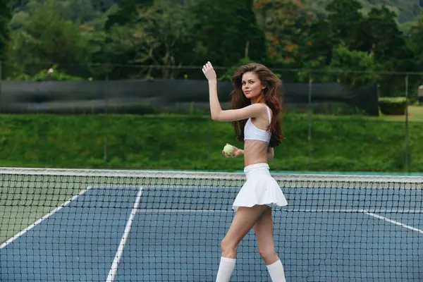 Şık beyaz tenis kıyafetli genç bir atletik kadın tenis kortunda poz verirken kendine güvenir, sağlıklı bir yaşam tarzı, spor ve yaz havasını temsil eder.