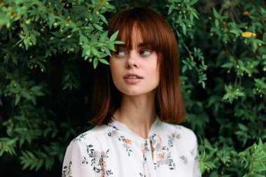 Canlı, kızıl saçlı bir kadın yemyeşil bir tarlada duruyor.