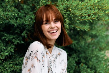 Neşeli bir ifadeyle yemyeşil bir yeşilin önünde oturan mutlu kızıl saçlı kadın.