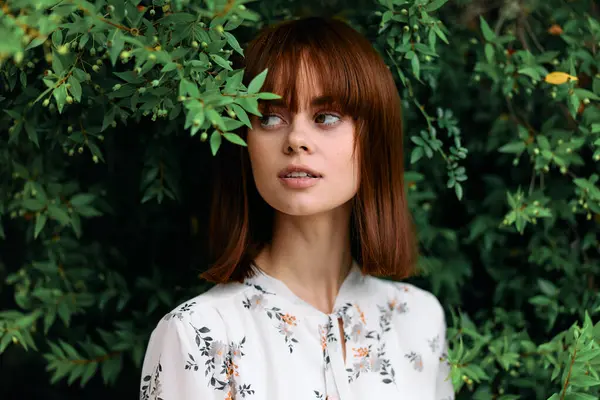 Canlı, kızıl saçlı bir kadın yemyeşil bir tarlada duruyor.