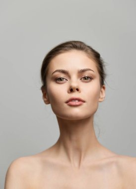 Minimalist bir portrede taze yüzlü bir kadın, yüz hatlarını ve doğal güzelliğini vurguluyor, pürüzsüz gri bir arkaplanda yumuşak bir ışıkta yakalanıyor..