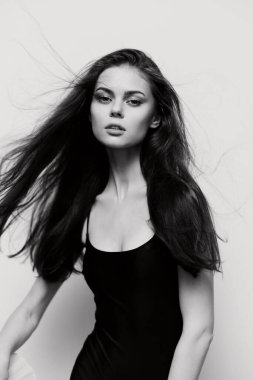 Şık, siyah bir elbise giyen, dalgalı saçlı zarif bir manken. Yüksek kontrastlı siyah-beyaz dekor onun özelliklerini vurguluyor, çarpıcı bir moda imajı yaratıyor..