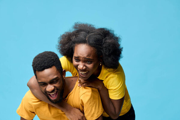 A happy couple in matching yellow outfits shares a playful moment, laughing joyfully against a vibrant blue backdrop, showcasing their love and connection