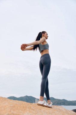 Formda genç bir kadın şık bir spor kıyafetle sahilde gezer, kendine güven ve canlılık gösterir, fitness, sağIık ve sağlıklı yaşam tarzı teması için idealdir.