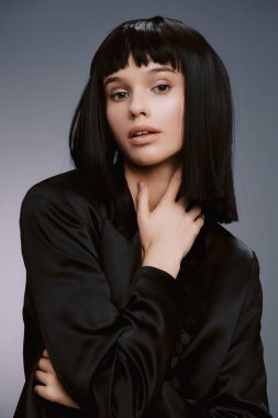 Siyah beyaz, siyah saçlı, siyah ceketli bir kadının stüdyo fotoğrafı, kameraya özgüvenle poz veriyor zarafet ve gücü vurgulayan bir portre.