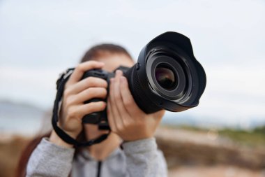 Genç bir kadın, DSLR kamera yeteneklerini güzel bir doğal arkaplan karşısında sergileyerek tutkulu bir şekilde açık hava fotoğrafçılığına girişiyor. Bu görüntü yaratıcılığı, heyecanı ve özünü yakalıyor.