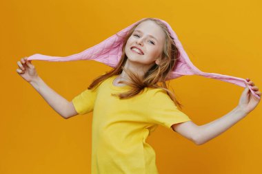Sarı tişörtlü ve pembe kapüşonlu neşeli genç kız, parlak sarı bir arka planda neşeyle gülümsüyor, mevsimlik çocuk modası ve mutluluk teması için mükemmel.