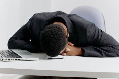 Takım elbiseli bir ofis çalışanı bir masanın üzerine yığılmış, kağıt yığınlarının altında gömülü, aşırı yorgunluk belirtileri gösteriyor..