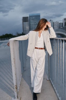 Şık bir iş kıyafeti giymiş kendine güvenen bir kadın, şehir zeminine karşı duruyor, dinamik ve şık bir ortamda profesyonelliğin ve modernliğin özünü yakalıyor..