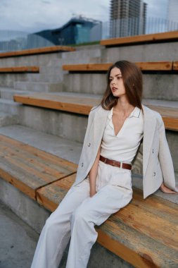 Şık bir takım elbise giymiş, kentte ahşap banklarda oturan kendine güvenen bir iş kadını, güçlendirmeyi, zarafeti ve profesyonel davranışı resmediyor..