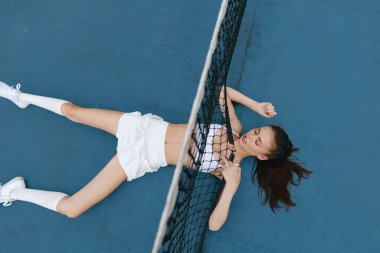 Yorgunluk ve kararlılığı somutlaştıran genç bir kadın tenis kortunda spor giysileri içinde canlı renkler ve atletik performans ve sporla ilgili enerjik duygular sergiliyor.