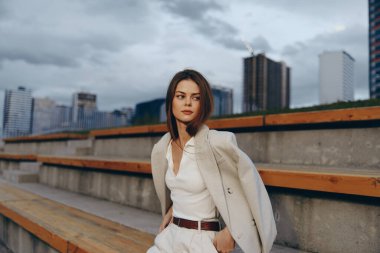 Dengeli bir iş kadını, çağdaş bir şehrin siluetine karşı durarak, hırs ve profesyonelliği sembolize ederek şık beyaz kıyafetine güvenini sergiliyor..