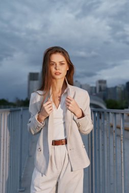 Şık bir iş elbisesi içindeki güçlü bir kadın, şehir silueti zeminine karşı güven yayıyor, kurumsal temalar için uygun güçlendirme ve profesyonelliği temsil ediyor..