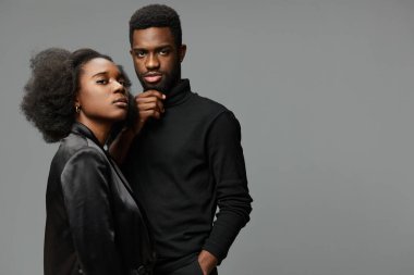 Doğal saç stili olan, şık siyah giyinen, zarif ve sofistike, minimalist gri bir ortamda yaşayan, çağdaş yaşam tarzı tasviri için mükemmel bir Afrikalı çift.