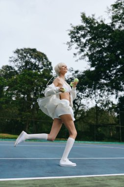 Tenis kortunda koşan şık beyaz kıyafetli enerjik genç bir manken, yemyeşil ve canlı bir ortamda neşe ve canlılık saçıyor.