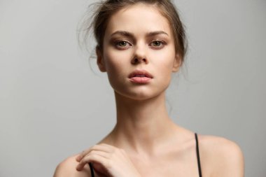 İfade eden bakışları ve yumuşak özellikleri olan genç bir kadın, doğal bir görünüm sergiliyor. Sessiz arka plan onun duruşu ve entelektüelliğini vurguluyor..