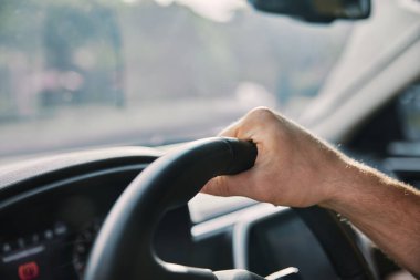 Sürücünün direksiyondaki el odaklı görüntüsü, aracın içini aydınlatan yumuşak güneş ışığıyla.