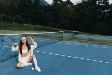 Spor kıyafetleri içinde enerjik genç bir kadın dışarıda tenisten zevk alıyor, neşe ve güven saçıyor, canlı bir mavi mahkemeye karşı yakalanmış, sporla ilgili konular için mükemmel.