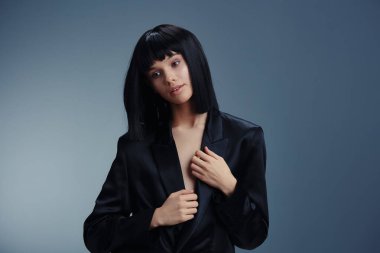 Siyah takım elbiseli kadın, elleri kalçasında poz veriyor, yan tarafa bakıyor, stüdyo ortamında güven ve profesyonellik yayıyor.