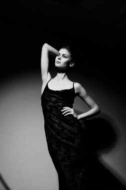 Sofistike bir kadın modelin siyah ve beyaz görüntüsü poz veriyor, zarafet ve modayı minimalist bir ortamda somutlaştırıyor. Ruh hali ve tarz kavramı.