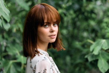 Çevresi gür yeşil ağaçlar ve bitkilerle çevrili kısa saçlı genç bir kadın.