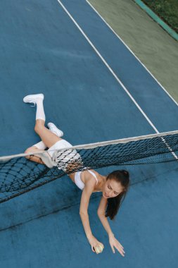 Sportif giyimli genç bir kadın, canlı bir mavi sahada topa yetişmeye çalışırken tenise olan bağlılığını gösteriyor. Güçlendirme ve sporu somutlaştırıyor.