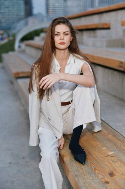 Ahşap basamaklarda oturan, kendine güveni olan, uzun saçlı ve sakin tavırlı, kurumsal ve profesyonel temalar için ideal, dengeli bir kadın..