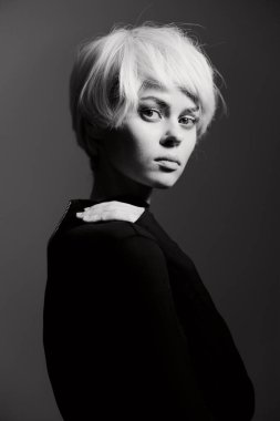 Zarif kısa sarı saçlı genç bir kadının büyüleyici siyah beyaz görüntüsü. Gösterişli, siyah bir kıyafet giymiş, düşünceli bir şekilde kameraya bakıyor, sanatsal özelliklerini yansıtıyor ve...