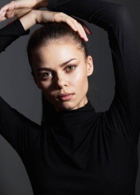 Şık, genç bir bayan model pozu ve ifadesi ile zarafet ve kendine güven gösteriyor. Koyu arkaplan onun özelliklerini vurguluyor, çarpıcı bir kontrast oluşturuyor.