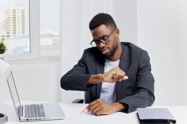 Afrikalı Amerikalı iş adamı yoğun bir şekilde düzenli bir ofis masasında, parlak bir dizüstü bilgisayar üzerinde çalışıyor, görevlerine konsantre oluyor..