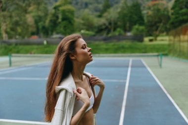 Tenis kortunda şık spor kıyafetler giyen atletik genç bir kadın, kendine güven ve rahatlama yayıyor, dingin yeşil bir ortamda, sakin bir atmosferde yaşıyor.