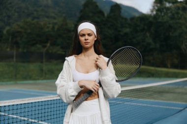 Spor kıyafetli enerjik genç bir kadın, sakin bir kortta tenis raketiyle güven içinde poz veriyor. Atletizmi, doğayı ve refahı temsil ediyor.
