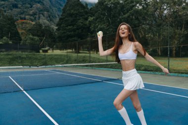 Dışarıda tenis oynayan neşeli genç bir kadın, spor bir kıyafet giyiyor, mutluluk ve enerji saçıyor, sağlıklı yaşam tarzı ve yaz sporları için mükemmel.